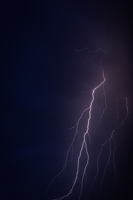 The image shows a dark night sky illuminated by a vivid lightning strike, with jagged, branching bolts piercing through the cloudless darkness. The lightning appears bright white with subtle bluish ti